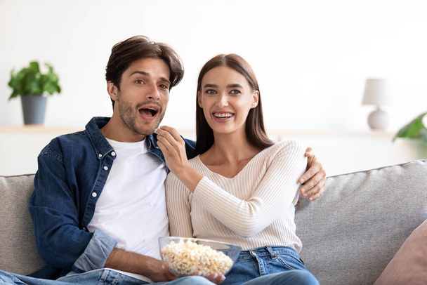 Sourire joyeux surpris heureux jeune couple européen manger du pop-corn et regarder un film drôle - Photo, image