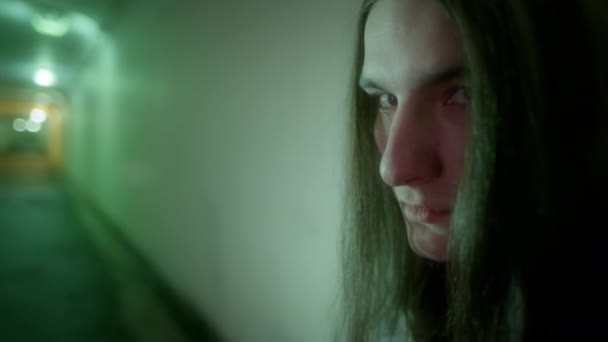 Homme aux cheveux longs regarde avec suspicion dans la lentille de la caméra dans un passage souterrain - Séquence, vidéo