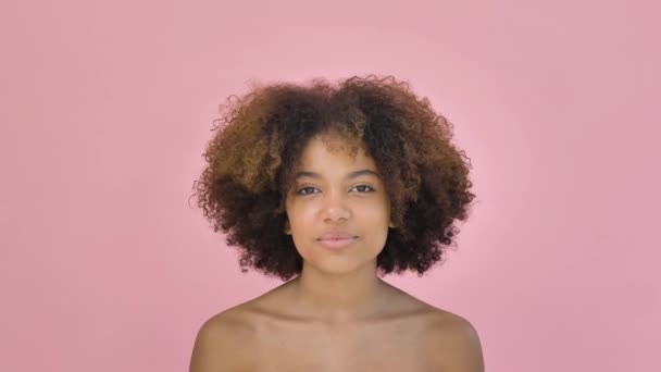 Πορτρέτο ενός χαριτωμένο Αφροαμερικανός γυναίκα κοιτάζοντας στην κάμερα και χαμογελώντας σε ένα ροζ φόντο - Πλάνα, βίντεο