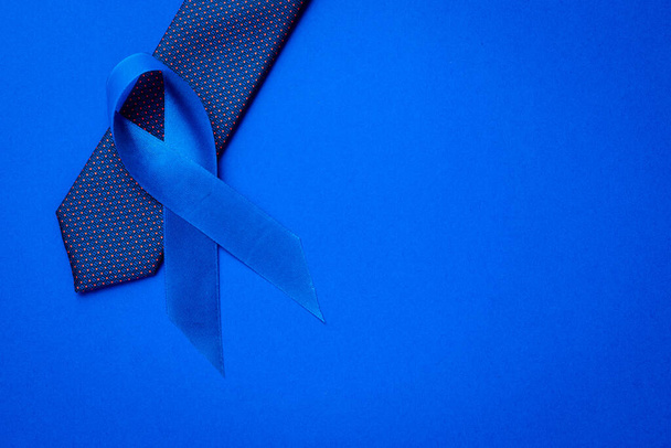 Ευαισθητοποίηση καρκίνου μπλε. Μπλε κορδέλα, γραβάτα που απομονώνεται σε βαθύ μπλε φόντο. Ευαισθητοποίηση του καρκίνου του προστάτη της υγείας των ανδρών το Νοέμβριο. Νοέμβριος και Διεθνής Ημέρα Mens - Φωτογραφία, εικόνα