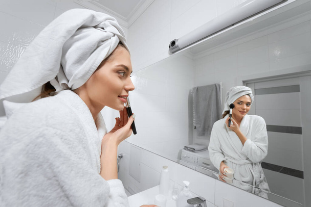 Happy confident young lady with towel on head doing makeup. - Fotografie, Obrázek