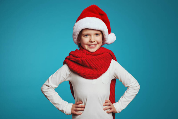 Strong confident girl in christmas hat and red scarf, holding hands on waist - Photo, Image