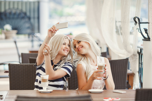 δύο κορίτσια να πιείτε τον καφέ και να χρησιμοποιήσετε το τηλέφωνο - Φωτογραφία, εικόνα