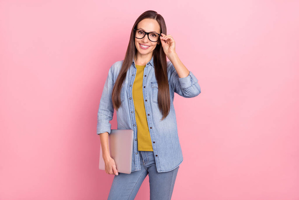 Photo of brunette cute young lady hold laptop wear spectacles jeans jacket isolated on pastel pink color background - Zdjęcie, obraz