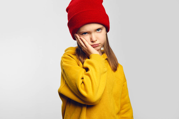 Tired girl makes face palm has gloomy expression wears yellow hoodie and red hat - Zdjęcie, obraz