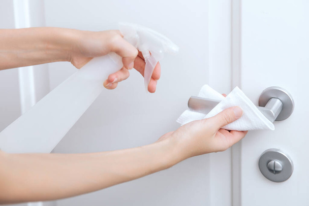Cleaning white door handles with an antiseptic wet wipe and sanitizer spray. Disinfection in hospital and public spaces against corona virus. Woman hand using towel for cleaning home room door link - Zdjęcie, obraz