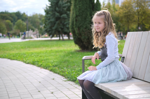 Portrait of pretty child girl sitting on park bench outdoors. - Photo, Image
