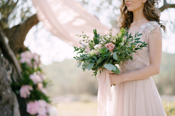 Невеста с букетом цветов в руках стоит под деревом. Крупный план - Фото, изображение