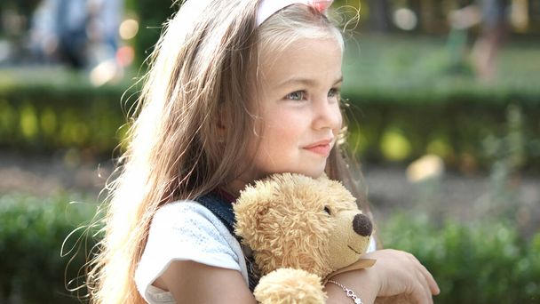 Happy little child girl playing with her favorite teddy bear toy outdoors in summer park. - Photo, Image