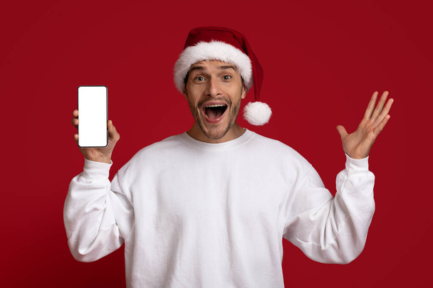Amazing Offer. Excited Guy In Santa Hat Holding Smartphone With Blank Screen - Φωτογραφία, εικόνα