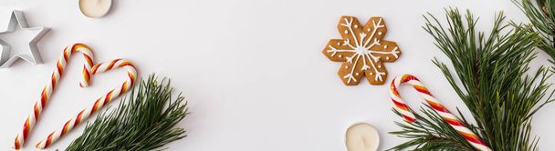 Christmas Banner. winter, new year composition. Christmas frame made of Fir tree branches, gingerbread, candles, candies on white background. Flat lay, top view, copy space - Photo, image