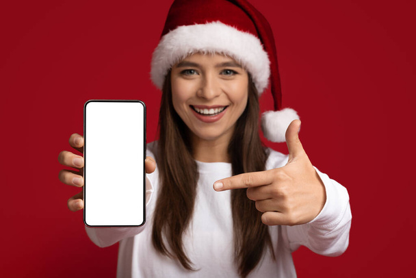 Holiday Promo. Cheerful Woman In Santa Hat Pointing At Blank Smartphone Screen - Foto, afbeelding