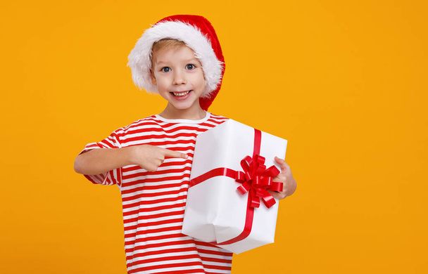 Overjoyed preschool lovely boy in red Santa hat pointing with finger on Christmas gift - Photo, image