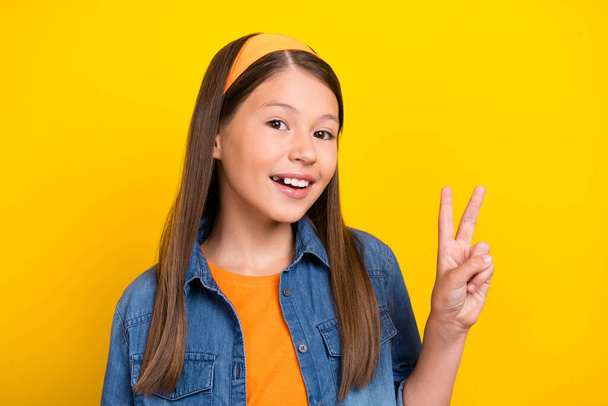 Photo of charming funky preteen girl dressed jeans shirt showing v-sign smiling isolated yellow color background - Фото, зображення