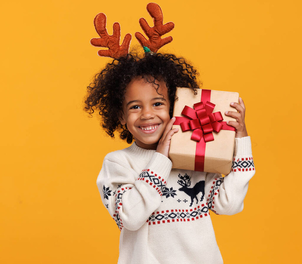 Noel tatili. Mutlu küçük Afrikalı Amerikalı çocuk Noel hediyesi kutulu kırmızı geyik boynuzu takıyor. - Fotoğraf, Görsel