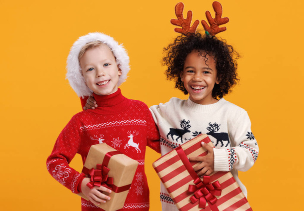 Szczęśliwy podekscytowany wielorasowe dzieci w Boże Narodzenie gospodarstwa prezenty Boże Narodzenie na żółtym tle - Zdjęcie, obraz