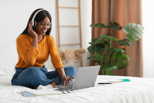 African Lady Using Laptop And Headphones Video Calling In Bedroom - Foto, afbeelding