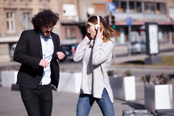 Young business colleagues dancing together with headphones after work. Happy friends jumping and fooling around outdoors. - Foto, imagen