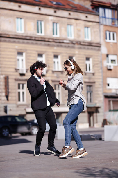 Young business colleagues dancing together with headphones after work. Happy friends jumping and fooling around outdoors. - Fotografie, Obrázek