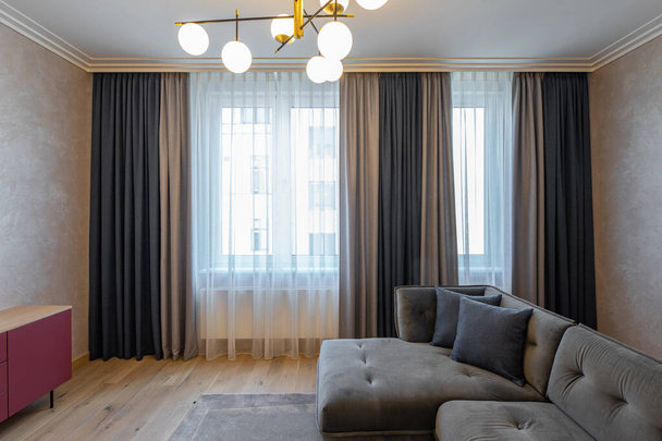 Modern interior of living room. Cozy grey sofa. Window with curtains. Stylish round lamps on chandelier. - Fotó, kép