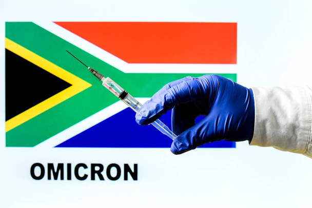 Seringa de mão com vacina vívida. Bandeira sul-africana e Omicron covid variante palavra escrita em segundo plano - Foto, Imagem