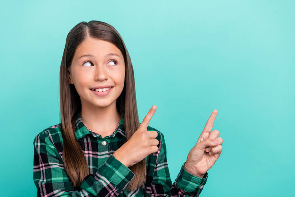 Photo of sweet adorable school girl dressed checkered clothes pointing two fingers looking empty space isolated teal color background - Foto, immagini