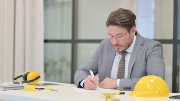 Μεσήλικας μηχανικός που γράφει σε χαρτί στο γραφείο - Πλάνα, βίντεο