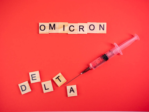 Wariant Omicron zastępuje Deltę. Pojawienie się nowego niebezpiecznego szczepu koronawirusa COVID-19 Omicron. Strzykawka. Słowa omicron delta na kolorowym czerwonym tle - Zdjęcie, obraz