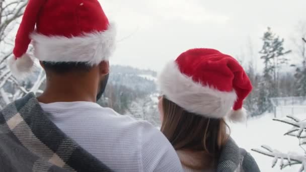 dos personas abrazándose en el invierno desde la colina con sombrero de Santas mirando a la distancia - Imágenes, Vídeo