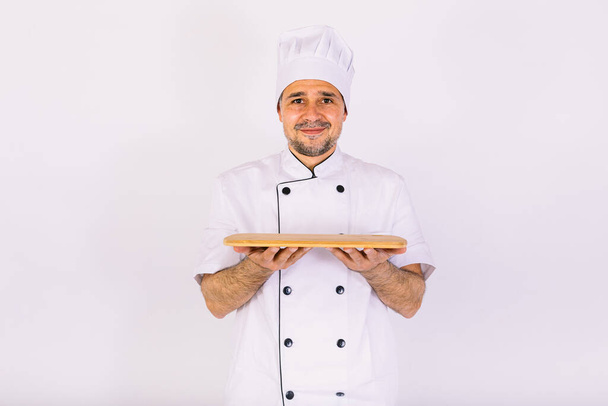 Chef cocinero con chaqueta de cocina y sombrero, sosteniendo una bandeja de madera, sobre fondo blanco - Foto, Imagen