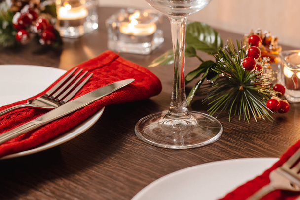 Різдвяний стіл. Тарілка та столові прибори на червоній серветці. Свічки горіли на столі напередодні Різдва. Готуємося до святкової вечері
.  - Фото, зображення