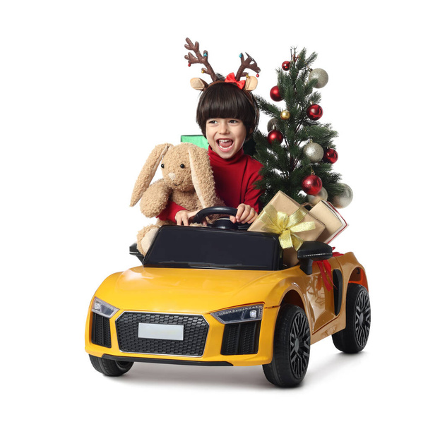 Cute little boy with Christmas tree, bunny toy and gift boxes driving children's car on white background - 写真・画像