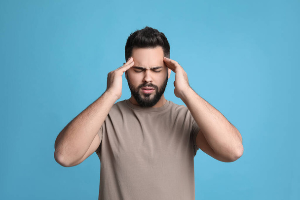 Young man suffering from headache on light blue background - Zdjęcie, obraz