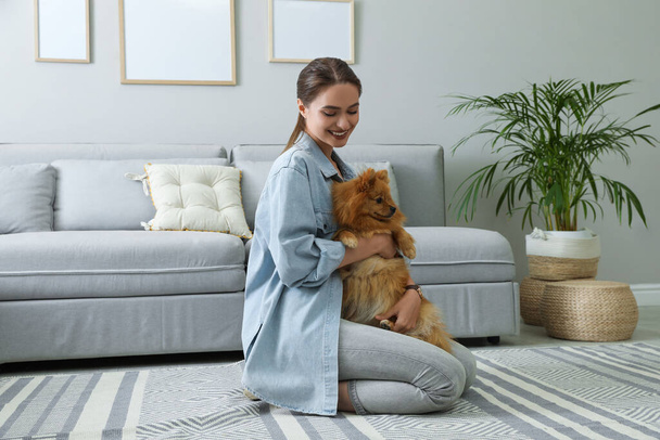 Happy young woman with cute dog in living room - Foto, Bild