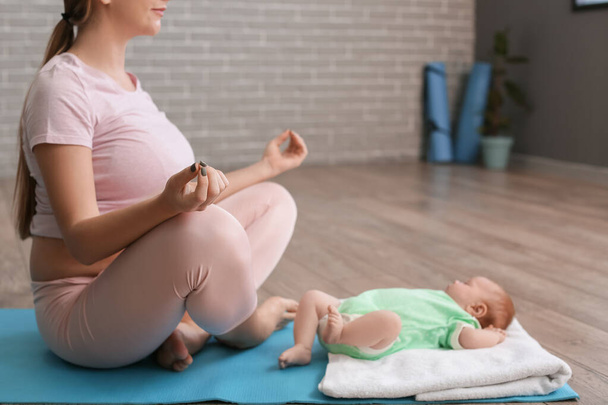Νεαρή έγκυος γυναίκα με μικρό μωρό διαλογίζεται στο γυμναστήριο - Φωτογραφία, εικόνα