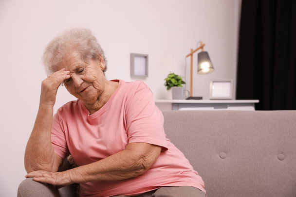 Femme âgée avec mal de tête assise sur le canapé à la maison. Espace pour le texte - Photo, image