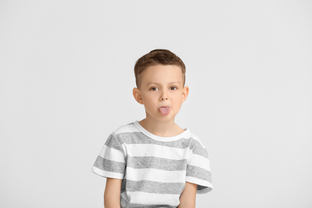 Portrait of cute little boy showing tongue on light background - Photo, Image