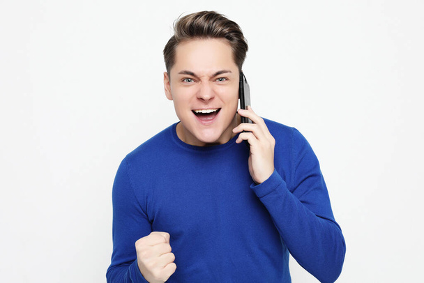 Happy young man in shirt gesturing and smiling while talking on the mobile phone - Foto, Imagem