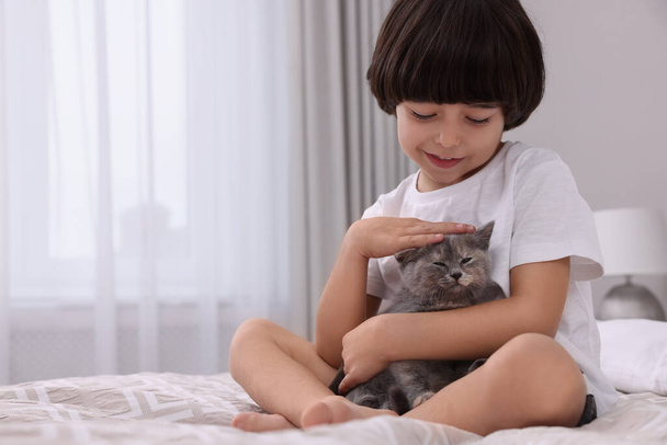 Cute little boy with kitten on bed at home. Childhood pet - Фото, изображение