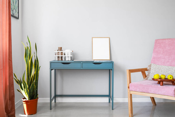 Kék asztal üres kerettel, kosárral, vázákkal és laptoppal a szoba falának közelében - Fotó, kép