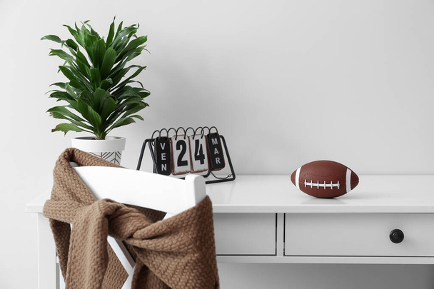 Rugby ball with calendar and houseplant on table near white wall - Фото, изображение