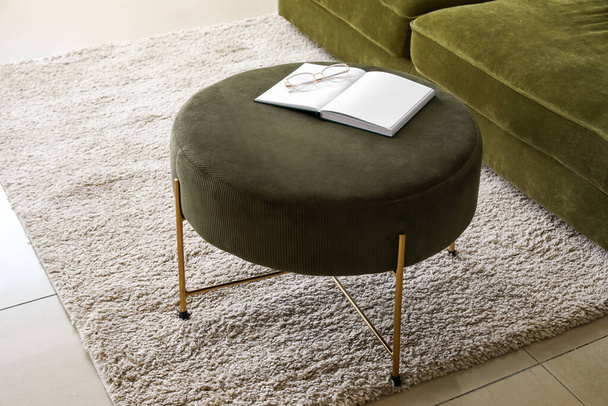 Open book with eyeglasses on green pouf in living room - Фото, зображення