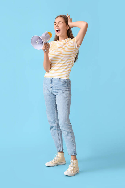 Emocional mujer joven gritando en megáfono sobre fondo azul - Foto, Imagen
