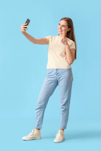 Mujer bonita con teléfono móvil tomando selfie sobre fondo azul - Foto, imagen