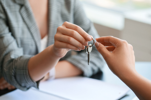 Агент з нерухомості дає ключ від будинку до клієнта в офісі, крупним планом
 - Фото, зображення