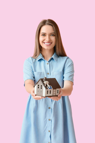 Smiling young woman with house model and keys on pink background - Photo, Image