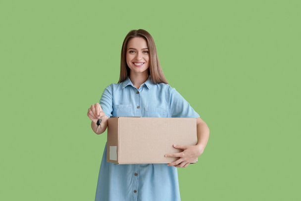 Smiling young woman with key from house and box on green background - Foto, afbeelding