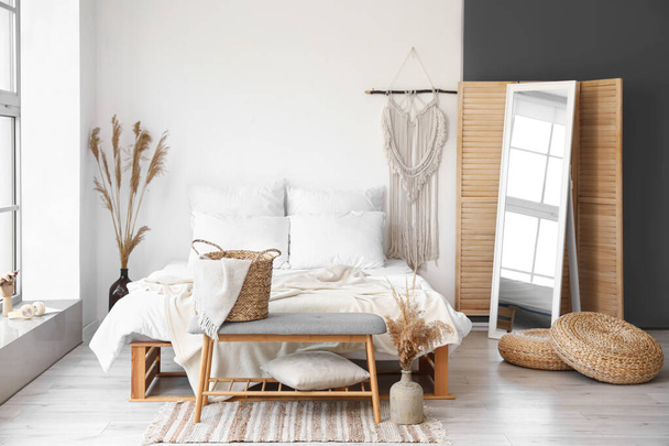 Interior of light bedroom with soft bench and dry reeds in vases - Foto, Imagen