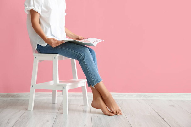Donna che legge una rivista su uno sgabello bianco vicino al muro rosa - Foto, immagini