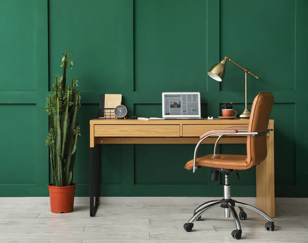Modern workplace with laptop near green wall in room - Фото, изображение